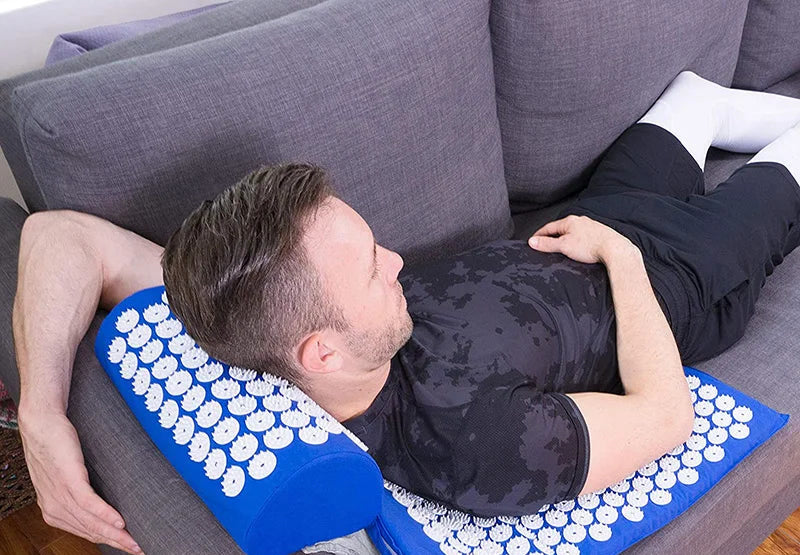 Man lying back on the blue acupressure mat and neck pillow on a sofa